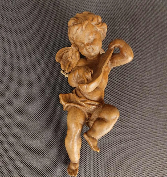 Jasna, drewniana rzeźba przedstawia pulchnego cherubinka grającego na mandolinie. Aniołek jest w ruchu, z uniesioną nogą i przechyloną głową. Widać małe skrzydła i krótkie, kręcone włosy. Całość emanuje radością i muzykalnością.