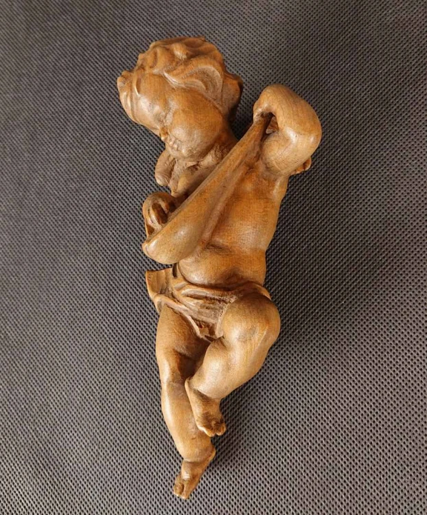 Jasna, drewniana rzeźba przedstawia pulchnego cherubinka grającego na mandolinie. Aniołek jest w ruchu, z uniesioną nogą i przechyloną głową. Widać małe skrzydła i krótkie, kręcone włosy. Całość emanuje radością i muzykalnością.
