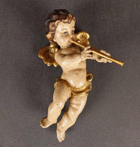 Drewniana rzeźba amorka w locie, z fletnią przy ustach. Polichromowana w odcieniach cielistych ze złoconymi skrzydełkami i szarfą. Urokliwa, barokowa stylistyka nadaje jej dekoracyjny, lekko sakralny charakter.