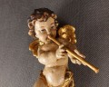Drewniana rzeźba amorka w locie, z fletnią przy ustach. Polichromowana w odcieniach cielistych ze złoconymi skrzydełkami i szarfą. Urokliwa, barokowa stylistyka nadaje jej dekoracyjny, lekko sakralny charakter.
