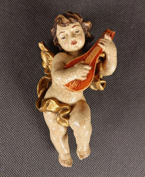 Przedstawiona rzeźba to niewielki, lecz niezwykle ekspresyjny putto – amorkowy posłaniec mitologii – zawieszony w ruchu podczas gry na lutni. Wykonany z drewna rzeźbiarski korpus emanuje autentycznym patynowaniem starej polichromii