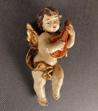 Przedstawiona rzeźba to niewielki, lecz niezwykle ekspresyjny putto – amorkowy posłaniec mitologii – zawieszony w ruchu podczas gry na lutni. Wykonany z drewna rzeźbiarski korpus emanuje autentycznym patynowaniem starej polichromii