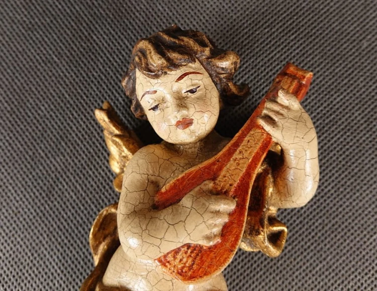 Przedstawiona rzeźba to niewielki, lecz niezwykle ekspresyjny putto – amorkowy posłaniec mitologii – zawieszony w ruchu podczas gry na lutni. Wykonany z drewna rzeźbiarski korpus emanuje autentycznym patynowaniem starej polichromii