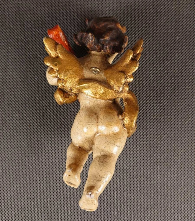 Przedstawiona rzeźba to niewielki, lecz niezwykle ekspresyjny putto – amorkowy posłaniec mitologii – zawieszony w ruchu podczas gry na lutni. Wykonany z drewna rzeźbiarski korpus emanuje autentycznym patynowaniem starej polichromii