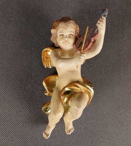 Polichromowana rzeźba z drewna przedstawia amorka ze skrzydełkami, unoszącego się w dynamicznej pozie i grającego na skrzypcach. Jego ciało ma jasną, cielistą barwę. Twarz amorka jest skierowana w stronę widza.