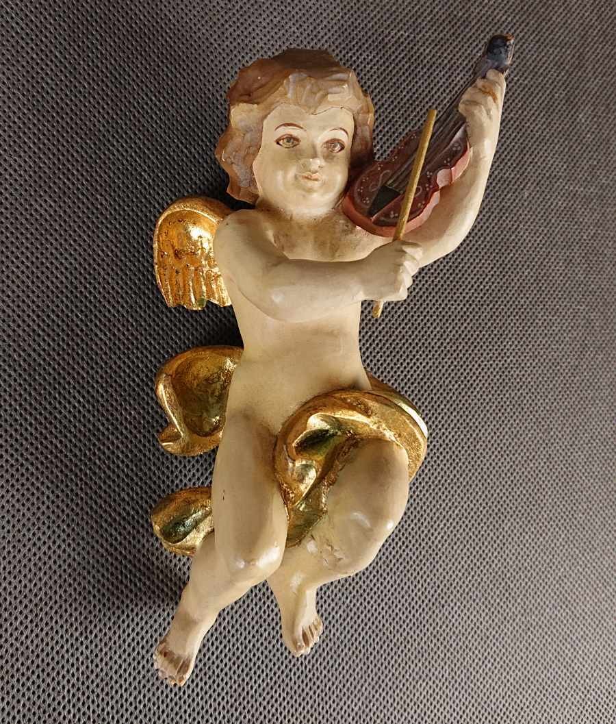 Polichromowana rzeźba z drewna przedstawia amorka ze skrzydełkami, unoszącego się w dynamicznej pozie i grającego na skrzypcach. Jego ciało ma jasną, cielistą barwę. Twarz amorka jest skierowana w stronę widza