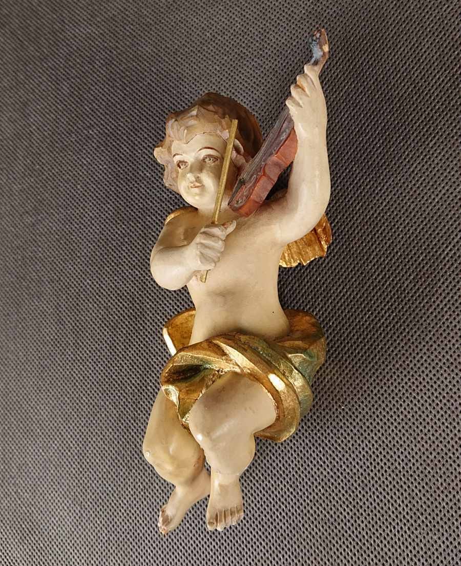 Polichromowana rzeźba z drewna przedstawia amorka ze skrzydełkami, unoszącego się w dynamicznej pozie i grającego na skrzypcach. Jego ciało ma jasną, cielistą barwę. Twarz amorka jest skierowana w stronę widza