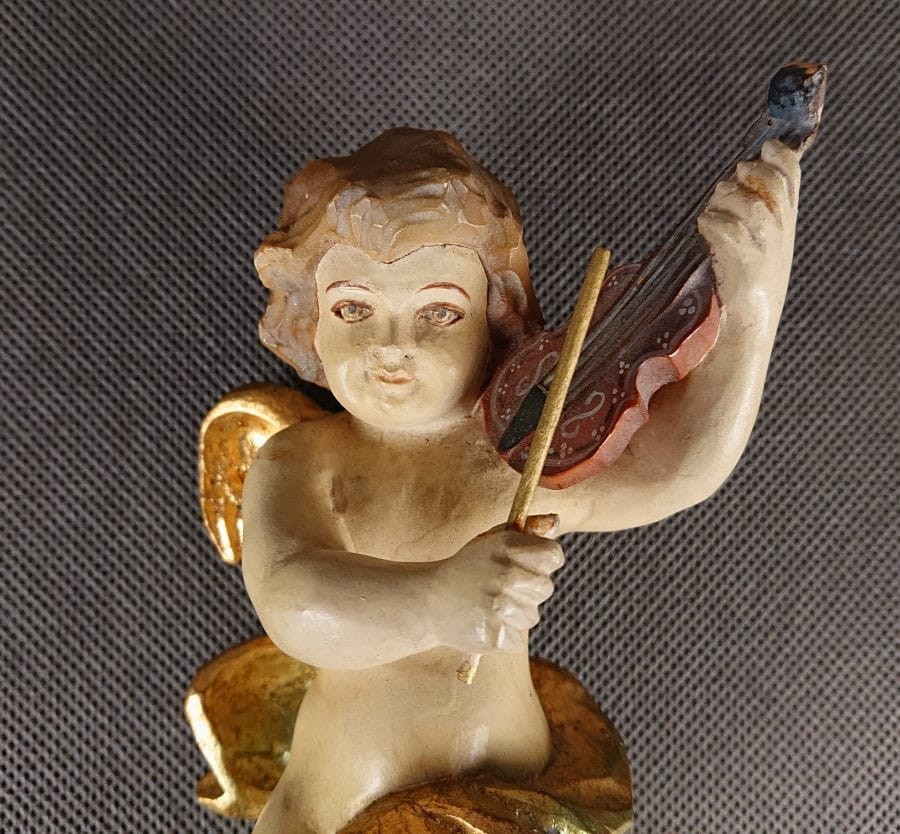 Polichromowana rzeźba z drewna przedstawia amorka ze skrzydełkami, unoszącego się w dynamicznej pozie i grającego na skrzypcach. Jego ciało ma jasną, cielistą barwę. Twarz amorka jest skierowana w stronę widza