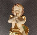 Polichromowana rzeźba z drewna przedstawia amorka ze skrzydełkami, unoszącego się i grającego na złotej trąbce. Jego ciało ma jasną, cielistą barwę. Włosy, w odcieniach brązu i złota, opadają mu lokami na ramiona