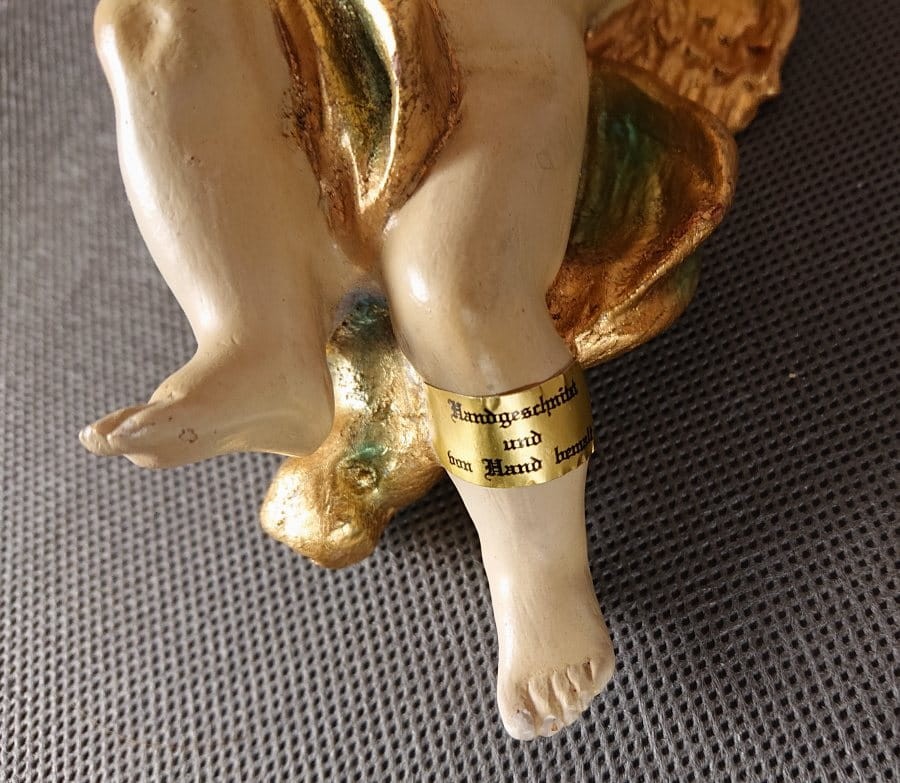 Polichromowana rzeźba z drewna przedstawia amorka ze skrzydełkami, unoszącego się i grającego na złotej trąbce. Jego ciało ma jasną, cielistą barwę. Włosy, w odcieniach brązu i złota, opadają mu lokami na ramiona