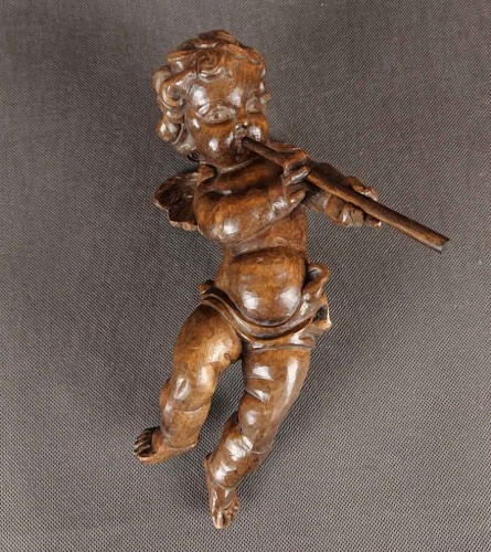 Duża rzeźba, ręcznie wykonana z jednego kawałka ciemnego, polerowanego drewna, ukazuje unoszącego się lekko aniołka w dynamicznej pozie. Smukłe, dziecięce ciało unosi się w powietrzu, wspierane przez subtelnie zarysowane skrzydełka o karbowanych piórach.