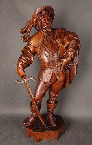 Duża, ręcznie wykonana rzeźba z drewna autorstwa Adalberta Steigelera z 1977 roku przedstawia postać mężczyzny w bogatym, historycznym stroju, inspirowanym XVII-wiecznym kawalerem lub muszkieterem. Rzeźba jest pełnoplastyczna i stoi na prostej podstawie.