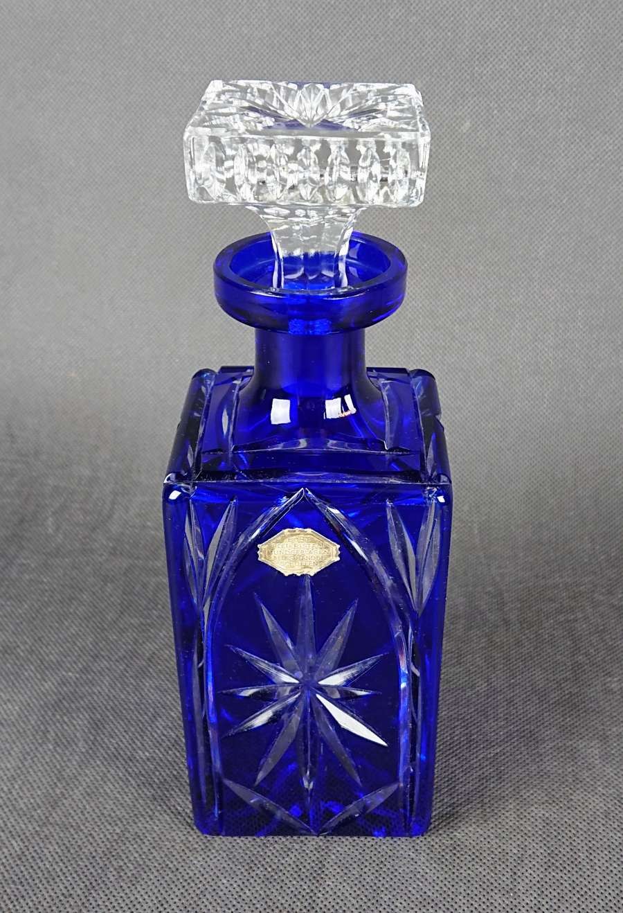 Karafka na alkohol z kryształu z motywami geometrycznymi ze szkła dwuwarstwowego ręcznie formowana i szlifowana, w kolorach bezbarwnym i kobaltowym. Ozdobiona szlifami w formie gwiazdy które kontrastują pomiędzy przezroczystą powierzchnią a kobaltową.