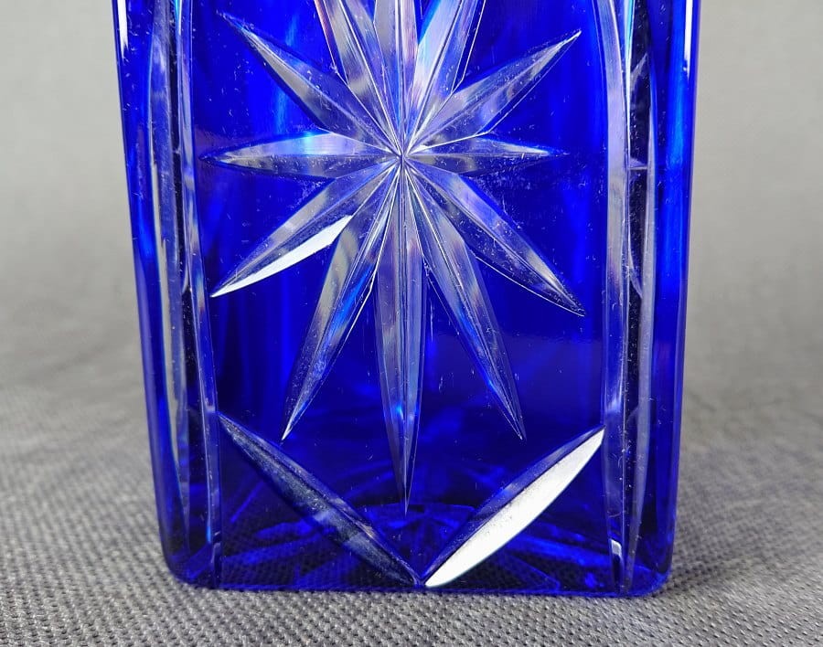 Karafka na alkohol z kryształu z motywami geometrycznymi ze szkła dwuwarstwowego ręcznie formowana i szlifowana, w kolorach bezbarwnym i kobaltowym. Ozdobiona szlifami w formie gwiazdy które kontrastują pomiędzy przezroczystą powierzchnią a kobaltową.