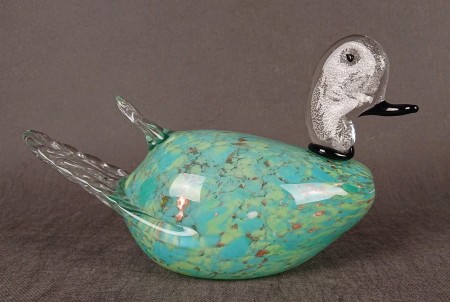 Duża figurka z wytwórni Murano przedstawia stylizowaną kaczkę, będącą przykładem mistrzowskiego kunsztu weneckich hutników szkła. Jej korpus ma opływowy kształt, wykonany z półprzezroczystego, turkusowego szkła z zatopionymi smugami brązowo-złotego pyłu.
