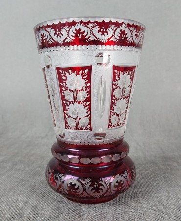 Ta szklanka w stylu Biedermeier, sygnowana "Krause 91", prezentuje charakterystyczną dla tego okresu elegancję i precyzję wykonania. Wykonana jest z rubinowego szkła, które intensywną, głęboką czerwienią przyciąga wzrok.