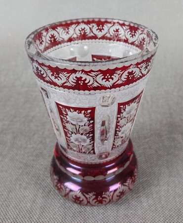 Ta szklanka w stylu Biedermeier, sygnowana "Krause 91", prezentuje charakterystyczną dla tego okresu elegancję i precyzję wykonania. Wykonana jest z rubinowego szkła, które intensywną, głęboką czerwienią przyciąga wzrok.