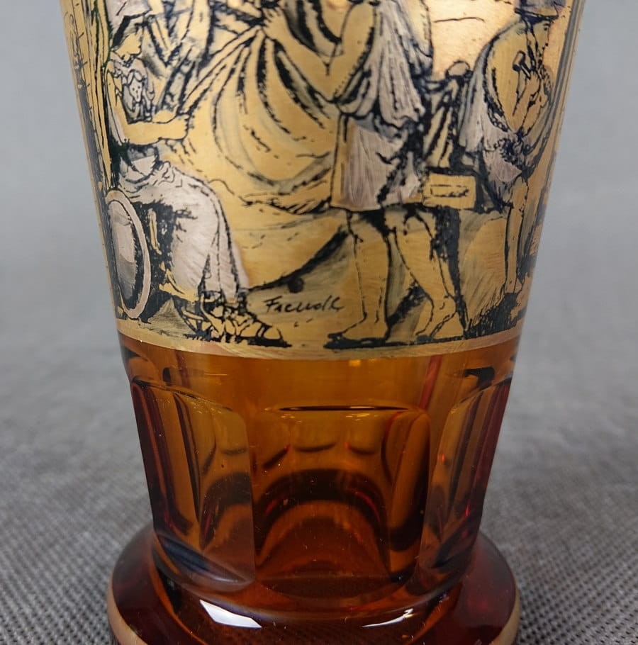 Szklanka, wykonana i ręcznie dekorowana w latach 20-30 XX wieku, prezentuje bogate zdobienie charakterystyczne dla tego okresu. Wykonana jest z miodowego, szkła, które w górnej partii jest matowione, tworząc kontrastującą powierzchnię dla dekoracji.