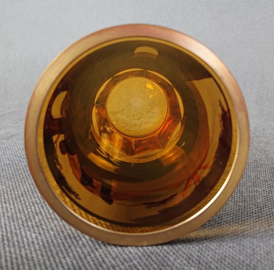 Szklanka, wykonana i ręcznie dekorowana w latach 20-30 XX wieku, prezentuje bogate zdobienie charakterystyczne dla tego okresu. Wykonana jest z miodowego, szkła, które w górnej partii jest matowione, tworząc kontrastującą powierzchnię dla dekoracji.