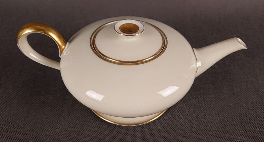 Wykonany z najwyższej jakości porcelany, imbryk do herbaty z podstawką z serwisu. Wykonany w renomowanej niemieckiej wytwórni porcelany, w pięknym odcieniu koloru ecru. Udekorowany imponującymi złoceniami.