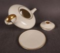 Wykonany z najwyższej jakości porcelany, imbryk do herbaty z podstawką z serwisu. Wykonany w renomowanej niemieckiej wytwórni porcelany, w pięknym odcieniu koloru ecru. Udekorowany imponującymi złoceniami.