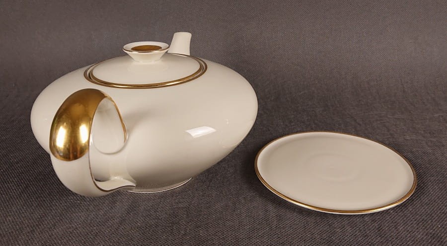 Wykonany z najwyższej jakości porcelany, imbryk do herbaty z podstawką z serwisu. Wykonany w renomowanej niemieckiej wytwórni porcelany, w pięknym odcieniu koloru ecru. Udekorowany imponującymi złoceniami.