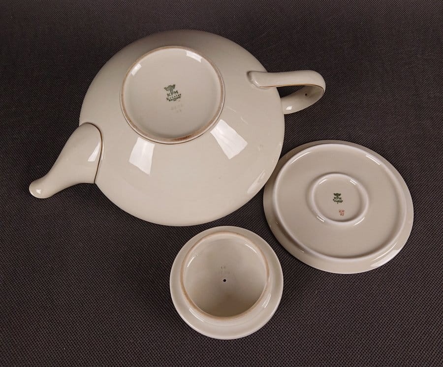 Wykonany z najwyższej jakości porcelany, imbryk do herbaty z podstawką z serwisu. Wykonany w renomowanej niemieckiej wytwórni porcelany, w pięknym odcieniu koloru ecru. Udekorowany imponującymi złoceniami.