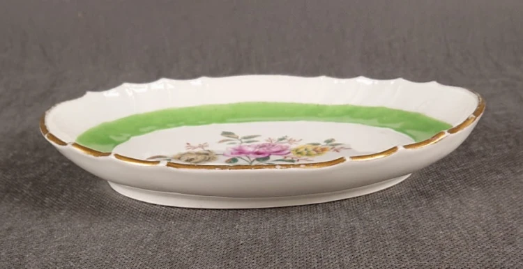 Porcelanowa patera z KPM Berlin, wykonana z białej szkliwionej porcelany, ma owalny kształt z falowanymi brzegami, nawiązującymi do stylu rokoko lub klasycystycznego. Krawędź patery jest podkreślona złoceniem, co dodaje jej elegancji.