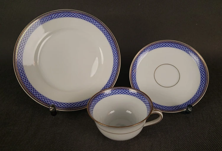 Zestaw śniadaniowy z fabryki porcelany C.M.Hutschenreuther składa się z filiżanki, spodka i talerza deserowego. Wszystkie elementy wykonane są z białej, szkliwionej porcelany i charakteryzują się geometrycznym zdobieniem w odcieniach błękitu i złota.