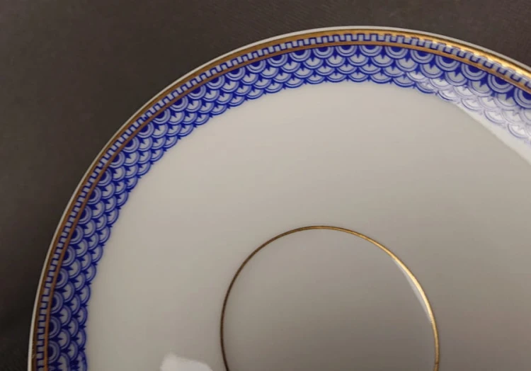 Zestaw śniadaniowy z fabryki porcelany C.M.Hutschenreuther składa się z filiżanki, spodka i talerza deserowego. Wszystkie elementy wykonane są z białej, szkliwionej porcelany i charakteryzują się geometrycznym zdobieniem w odcieniach błękitu i złota.