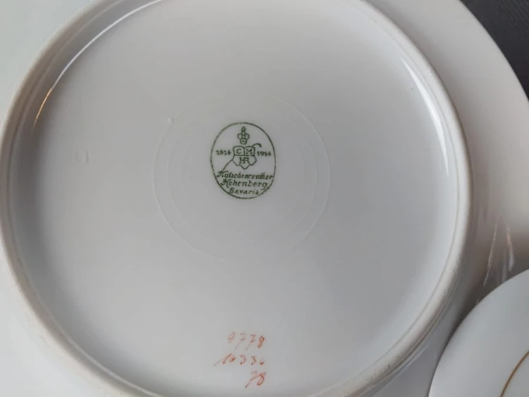 Zestaw śniadaniowy z fabryki porcelany C.M.Hutschenreuther składa się z filiżanki, spodka i talerza deserowego. Wszystkie elementy wykonane są z białej, szkliwionej porcelany i charakteryzują się geometrycznym zdobieniem w odcieniach błękitu i złota.