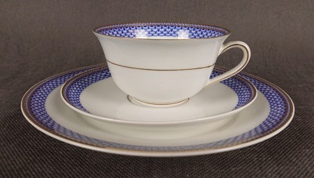 Zestaw śniadaniowy z fabryki porcelany C.M.Hutschenreuther składa się z filiżanki, spodka i talerza deserowego. Wszystkie elementy wykonane są z białej, szkliwionej porcelany i charakteryzują się geometrycznym zdobieniem w odcieniach błękitu i złota.