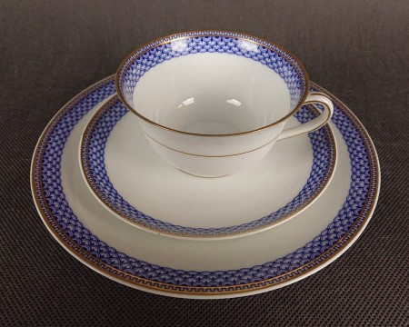Zestaw śniadaniowy z fabryki porcelany C.M.Hutschenreuther składa się z filiżanki, spodka i talerza deserowego. Wszystkie elementy wykonane są z białej, szkliwionej porcelany i charakteryzują się geometrycznym zdobieniem w odcieniach błękitu i złota.