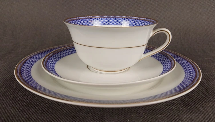 Zestaw śniadaniowy z fabryki porcelany C.M.Hutschenreuther składa się z filiżanki, spodka i talerza deserowego. Wszystkie elementy wykonane są z białej, szkliwionej porcelany i charakteryzują się geometrycznym zdobieniem w odcieniach błękitu i złota.