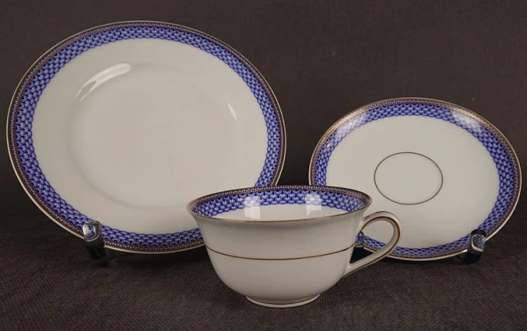 Zestaw śniadaniowy z fabryki porcelany C.M.Hutschenreuther składa się z filiżanki, spodka i talerza deserowego. Wszystkie elementy wykonane są z białej, szkliwionej porcelany i charakteryzują się geometrycznym zdobieniem w odcieniach błękitu i złota.