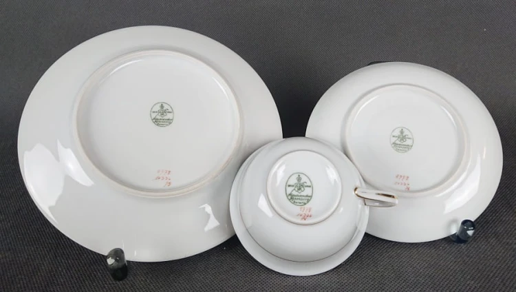 Zestaw śniadaniowy z fabryki porcelany C.M.Hutschenreuther składa się z filiżanki, spodka i talerza deserowego. Wszystkie elementy wykonane są z białej, szkliwionej porcelany i charakteryzują się geometrycznym zdobieniem w odcieniach błękitu i złota.
