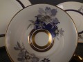 Przedwojenny zestaw śniadaniowy z niemieckiej fabryki porcelany Hertel Jacob. składa się z filiżanki, spodka i talerza deserowego. Zestaw charakteryzuje się elegancką, kremową porcelaną oraz delikatnymi zdobieniami w odcieniach błękitu, szarości i złota.