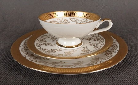 Porcelanowy zestaw śniadaniowy z niemieckiej fabryki Hertel Jacob & Co. to elegancki komplet składający się z filiżanki, spodka i talerza deserowego. Wykonana z białej, szkliwionej porcelany i bogato zdobiona złotymi, reliefowymi i malowanymi wzorami.