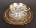 Porcelanowy zestaw śniadaniowy z niemieckiej fabryki Hertel Jacob & Co. to elegancki komplet składający się z filiżanki, spodka i talerza deserowego. Wykonana z białej, szkliwionej porcelany i bogato zdobiona złotymi, reliefowymi i malowanymi wzorami.