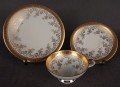 Porcelanowy zestaw śniadaniowy z niemieckiej fabryki Hertel Jacob & Co. to elegancki komplet składający się z filiżanki, spodka i talerza deserowego. Wykonana z białej, szkliwionej porcelany i bogato zdobiona złotymi, reliefowymi i malowanymi wzorami.