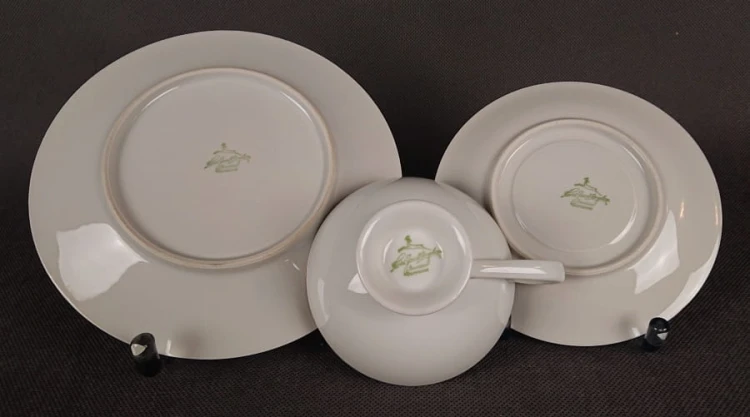 Porcelanowy zestaw śniadaniowy z niemieckiej fabryki Hertel Jacob & Co. to elegancki komplet składający się z filiżanki, spodka i talerza deserowego. Wykonana z białej, szkliwionej porcelany i bogato zdobiona złotymi, reliefowymi i malowanymi wzorami.