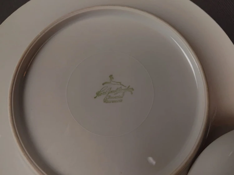 Porcelanowy zestaw śniadaniowy z niemieckiej fabryki Hertel Jacob & Co. to elegancki komplet składający się z filiżanki, spodka i talerza deserowego. Wykonana z białej, szkliwionej porcelany i bogato zdobiona złotymi, reliefowymi i malowanymi wzorami.