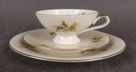 Zestaw śniadaniowy z niemieckiej fabryki porcelany Hertel Jacob & Co. to elegancki komplet składający się z filiżanki, spodka i talerza deserowego. Elementy wykonane są z białej, szkliwionej porcelany i zdobione motywami ostów i złotymi akcentami.