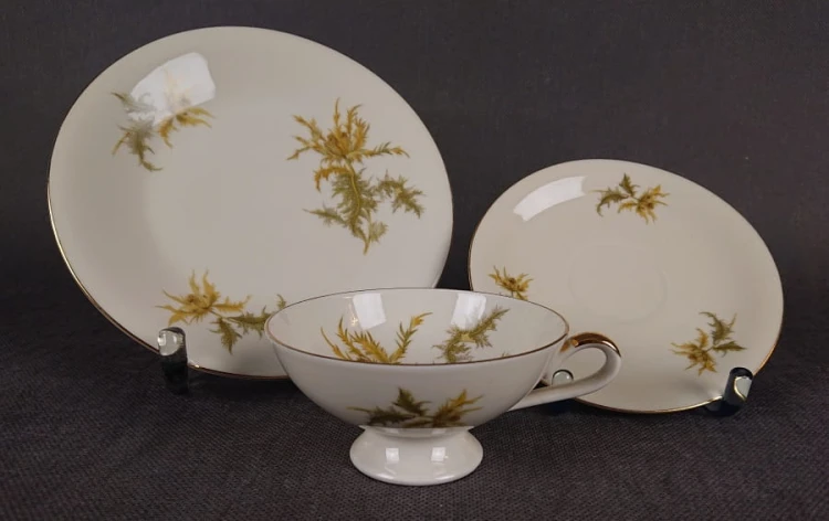 Zestaw śniadaniowy z niemieckiej fabryki porcelany Hertel Jacob & Co. to elegancki komplet składający się z filiżanki, spodka i talerza deserowego. Elementy wykonane są z białej, szkliwionej porcelany i zdobione motywami ostów i złotymi akcentami.