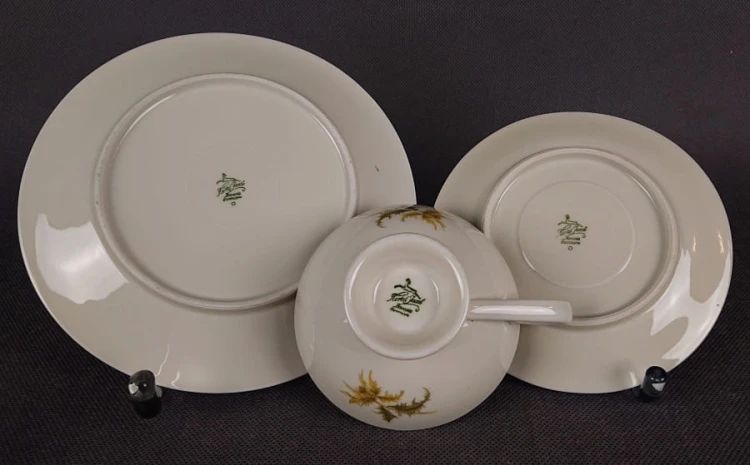 Zestaw śniadaniowy z niemieckiej fabryki porcelany Hertel Jacob & Co. to elegancki komplet składający się z filiżanki, spodka i talerza deserowego. Elementy wykonane są z białej, szkliwionej porcelany i zdobione motywami ostów i złotymi akcentami.