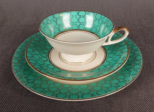 Śliczny zestaw śniadaniowy, o pięknych klasycznych kształtach. Wykonany z bardzo wysokiej klasy porcelany w kolorze ecru. Zestaw składa się z talerzyka deserowego, spodka i filiżanki. Udekorowana na zielonym tle bogatymi złoconymi.