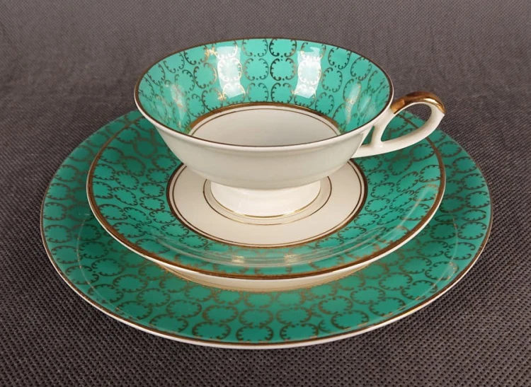 Śliczny zestaw śniadaniowy, o pięknych klasycznych kształtach. Wykonany z bardzo wysokiej klasy porcelany w kolorze ecru. Zestaw składa się z talerzyka deserowego, spodka i filiżanki. Udekorowana na zielonym tle bogatymi złoconymi.