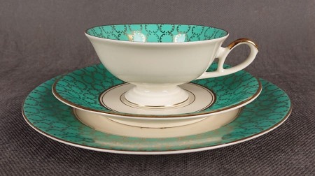 Śliczny zestaw śniadaniowy, o pięknych klasycznych kształtach. Wykonany z bardzo wysokiej klasy porcelany w kolorze ecru. Zestaw składa się z talerzyka deserowego, spodka i filiżanki. Udekorowana na zielonym tle bogatymi złoconymi.