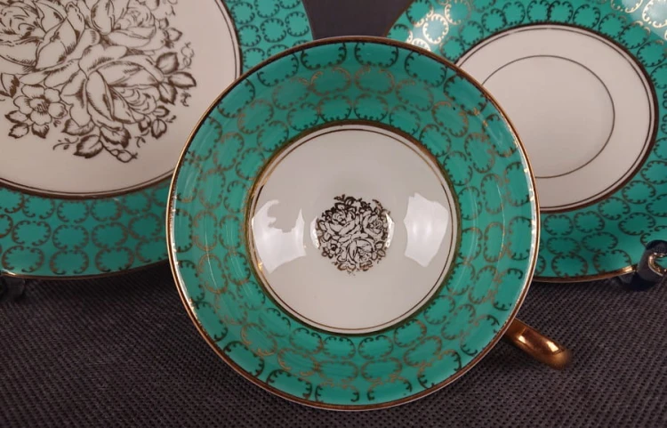 Śliczny zestaw śniadaniowy, o pięknych klasycznych kształtach. Wykonany z bardzo wysokiej klasy porcelany w kolorze ecru. Zestaw składa się z talerzyka deserowego, spodka i filiżanki. Udekorowana na zielonym tle bogatymi złoconymi.