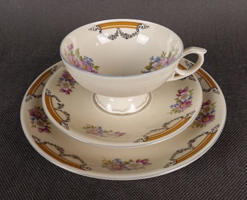 Zestaw niemieckiej firmy Johann Seltmann z lat 40. XX w. składa się z filiżanki, małego spodka i talerzyka deserowego. Wykonany z kremowej porcelany. Wnętrze filiżanki i ranty talerzy zdobią delikatne girlandy kwiatów w odcieniach lila, różu i błękitu.